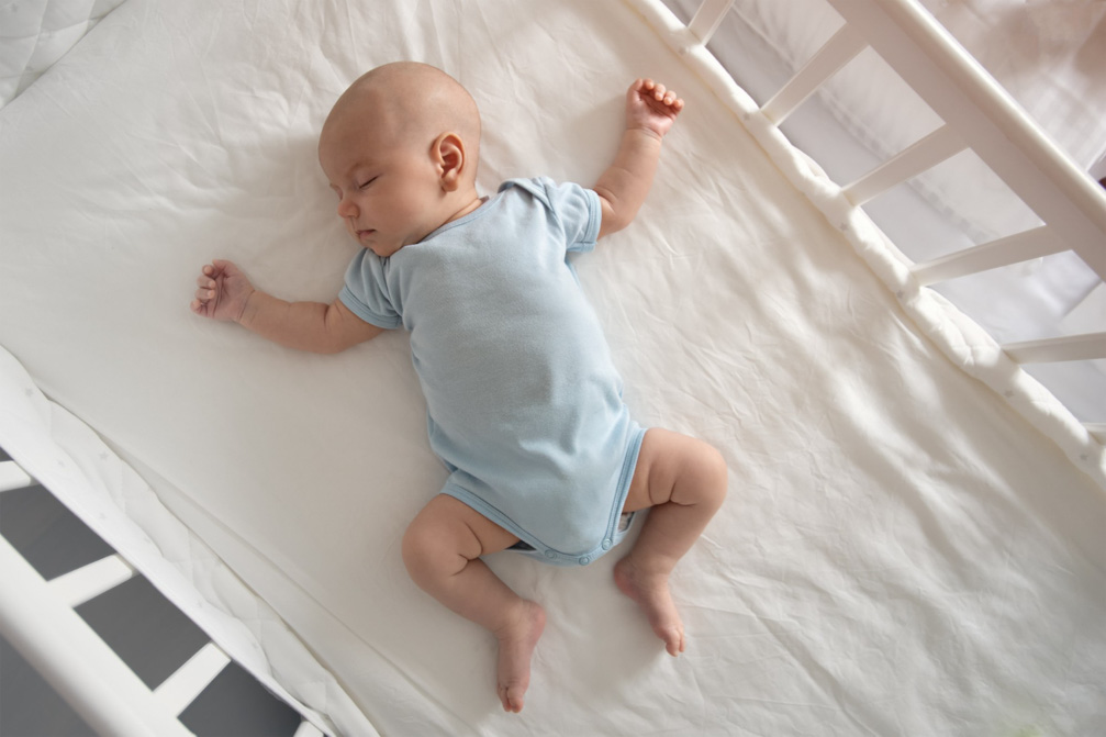 Μωρό με γαλάζια πυτζαμάκια κοιμάται ανάσκελα μέσα σε μια ευρύχωρη κούνια.