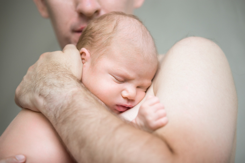 Νεαρός μπαμπάς κάνει επαφή δέρμα με δέρμα με το νεογέννητο μωρό του, κρατώντας το στην αγκαλιά του.