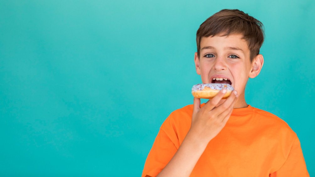 Παιδικός διαβήτης και διατροφή. Αγοράκι με πορτοκαλί μπλούζα τρώει έναν λουκουμά με λευκή σοκολάτα.