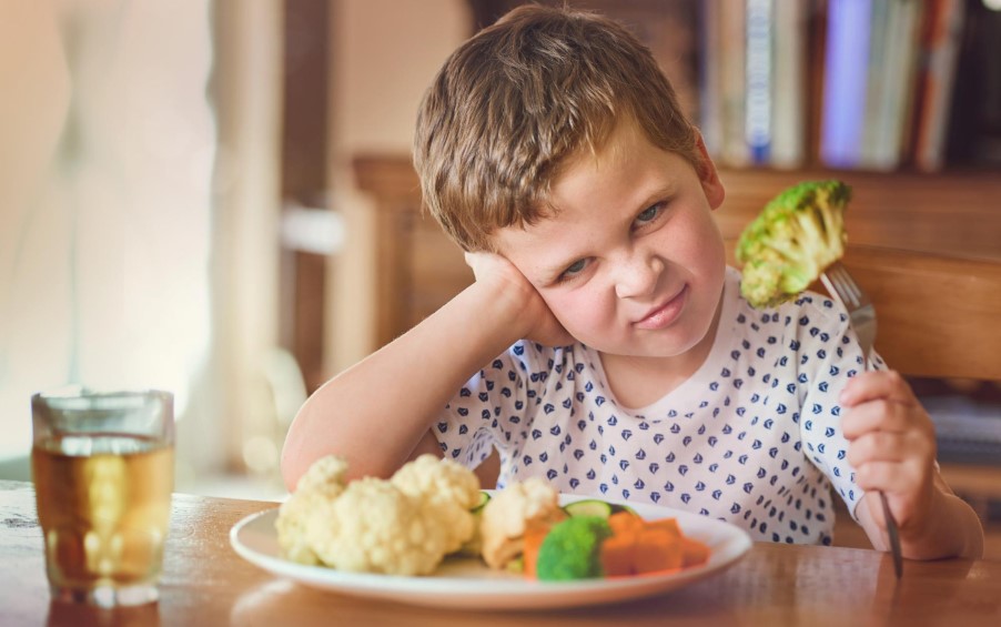 Μικρό αγόρι κάθεται στο τραπέζι και κοιτάει αηδιασμένο τα λαχανικά τα οποία αρνείται να φάει.